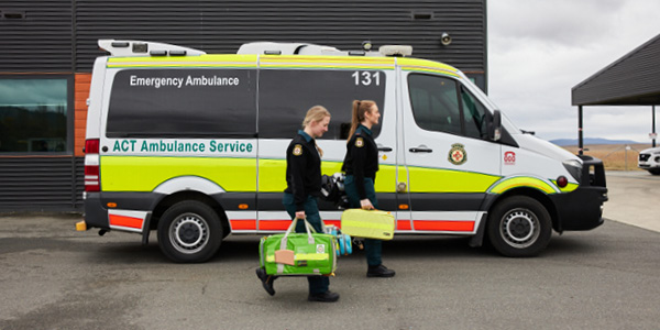 Two paramedics carrying a bag each walking pass an ambulance